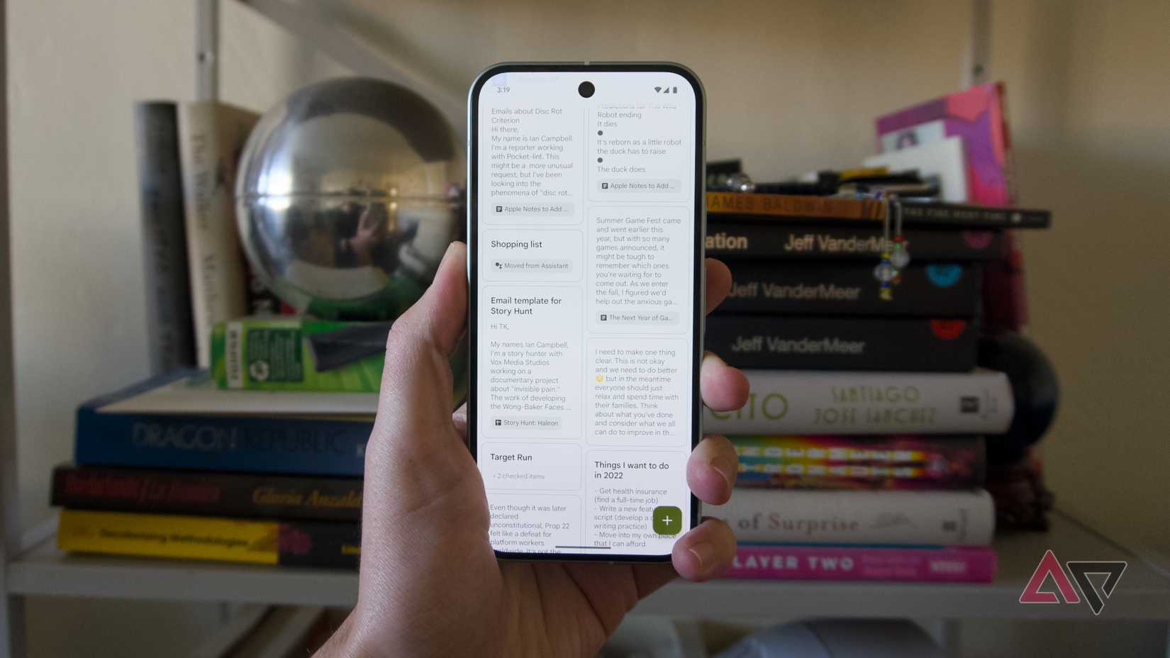 Uma mão segurando um Pixel 9 com o Google Keep em frente a uma estante.