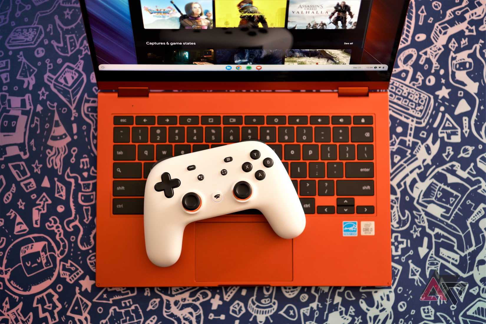 A white Google Stadia controller sitting on the keyboard of a red Chromebook with a gaming service open on the screen. The laptop is sitting on a blue background with silver graphics of video game images.