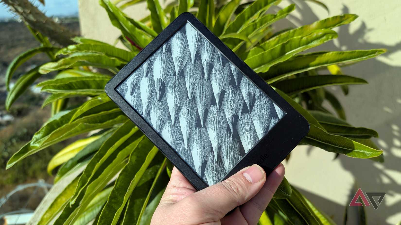 Amazon Kindle 2024 em mãos em frente a uma planta frondosa