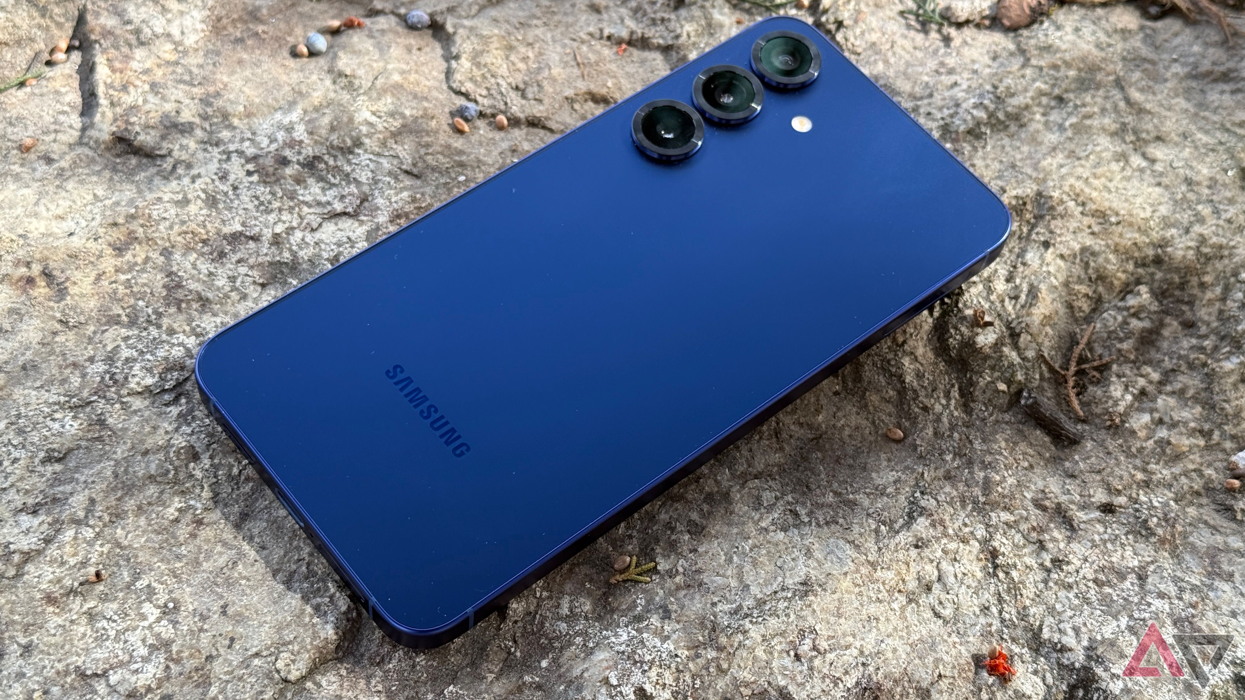 A blue Samsung Galaxy S25+ rests face down on a rock