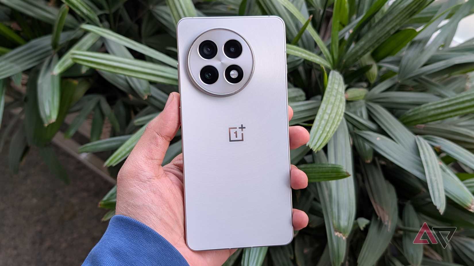OnePlus 13R mantido na posição vertical, mostrando o design da câmera traseira em ambientes externos