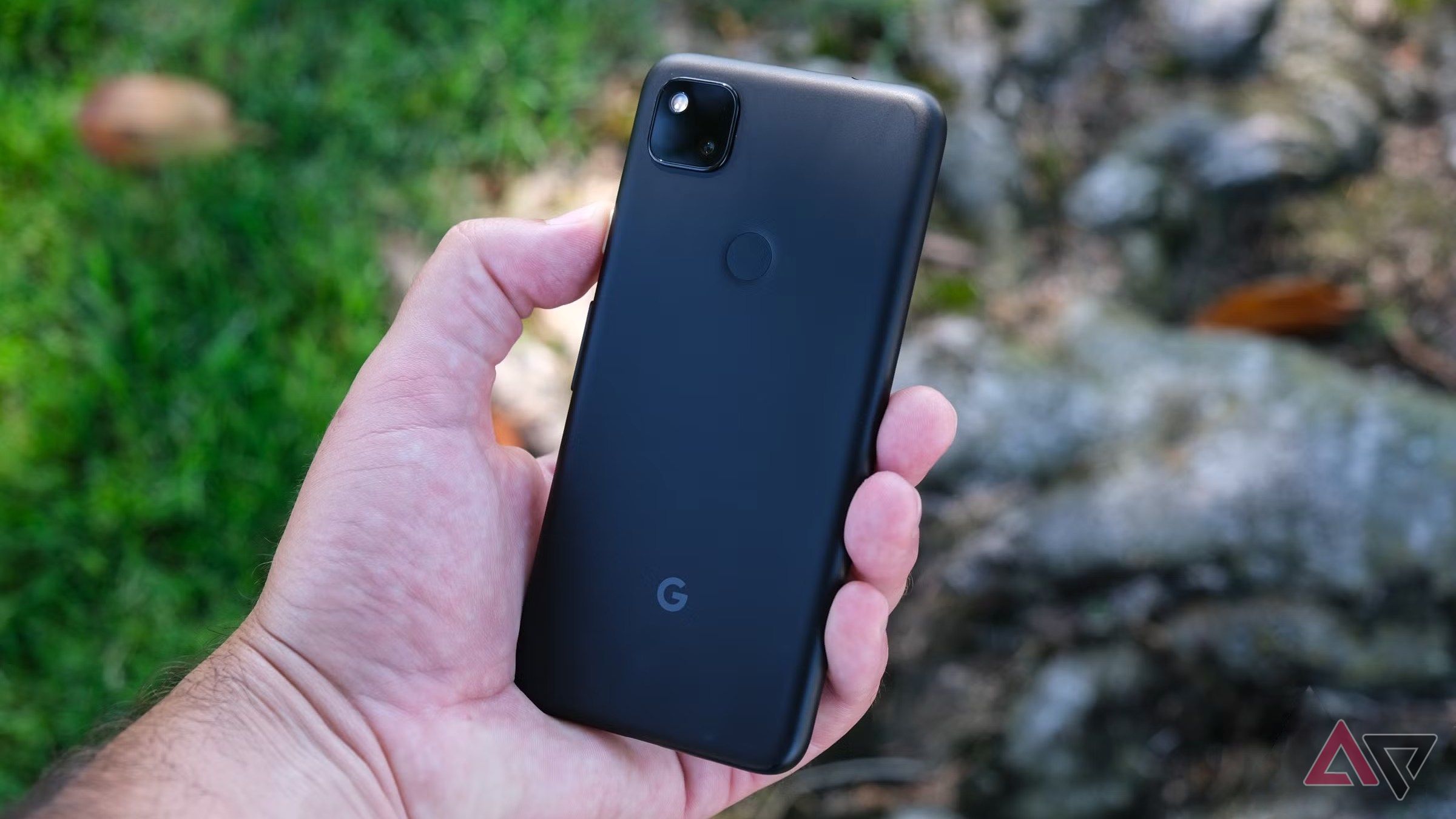 A Pixel 4a held in a hand outdoors.