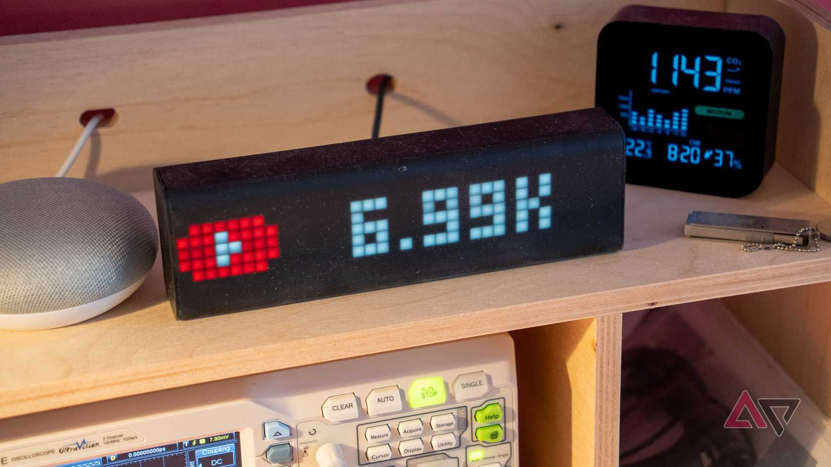 a lametric time smart clock on a wooden shelf displaying youtube subscriber counter next to a google home mini and a home CO2 meter