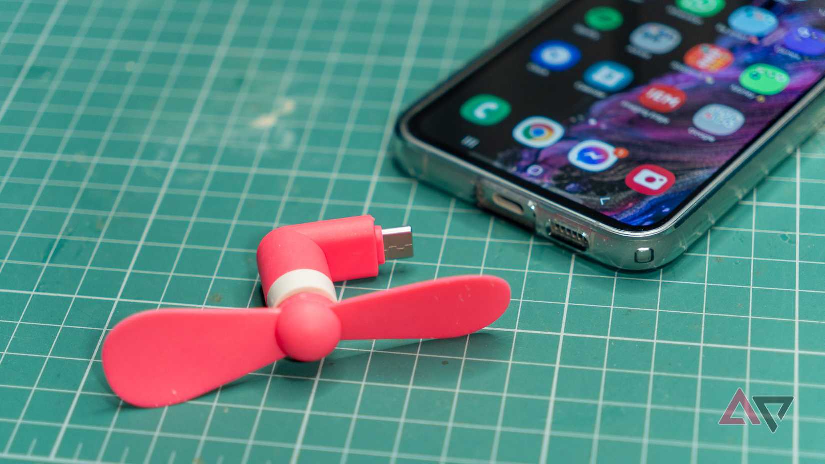 a pink usb fan next to a samsung phone on a green mat