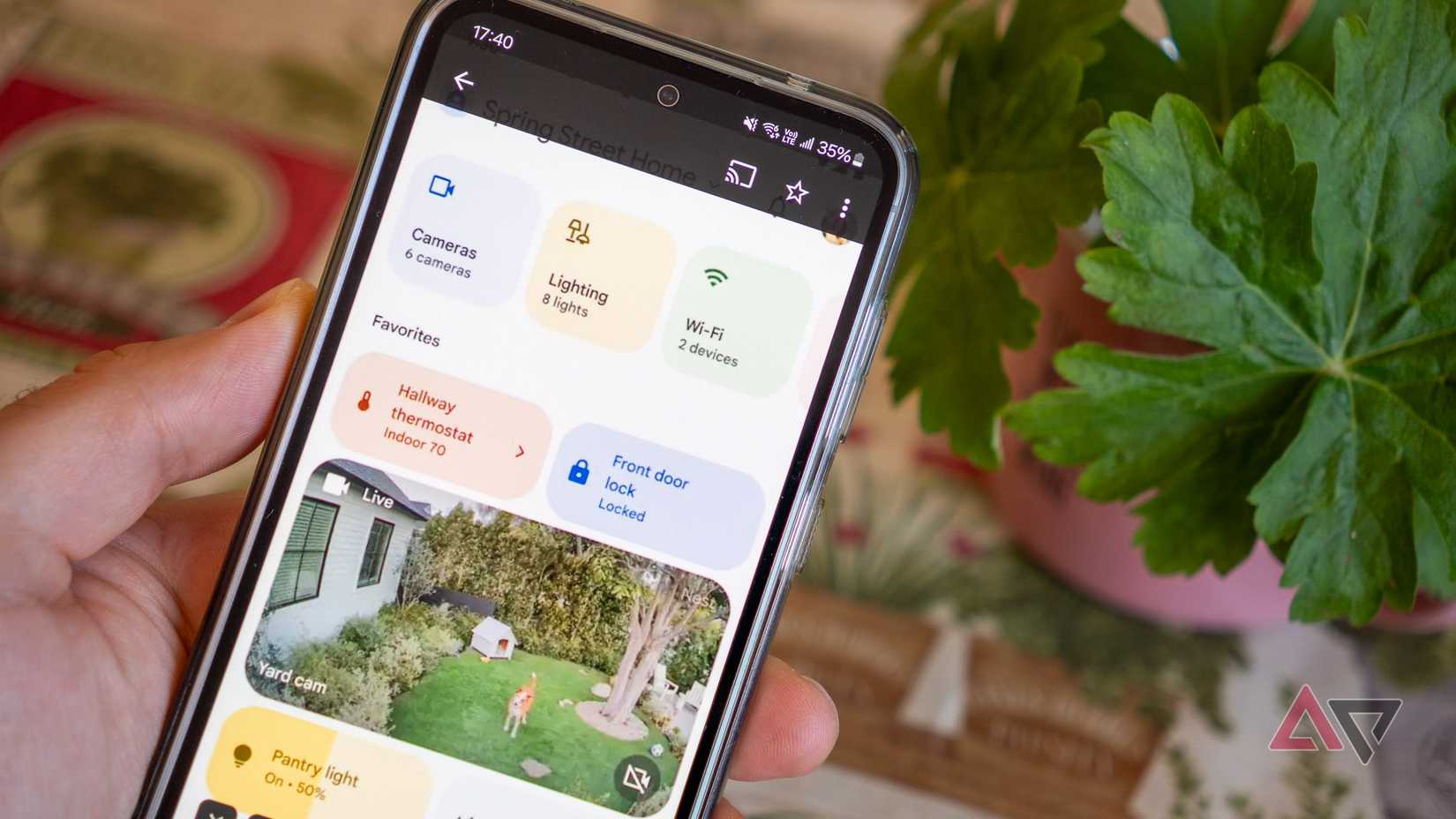 um telefone na mão exibindo um painel de casa inteligente ao lado de uma planta