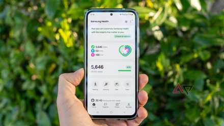 un telefono in mano che mostra la schermata iniziale dell'app Samsung Health con cespugli sullo sfondo