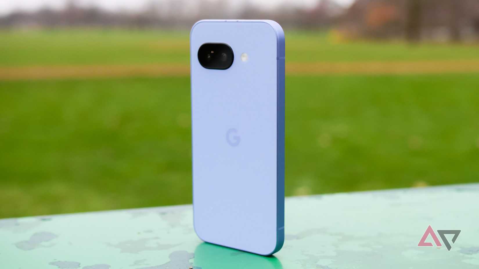 The Google Pixel 9a standing upright in a park, with the purple back showing towards the camera.