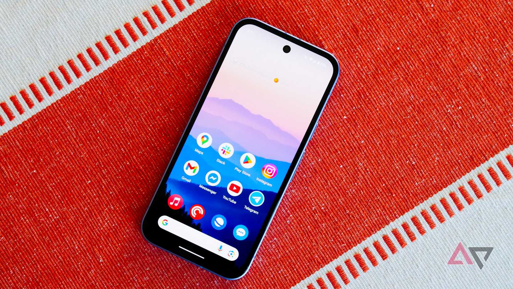The Pixel 9a on an orange and white backdrop with the display on and facing up.
