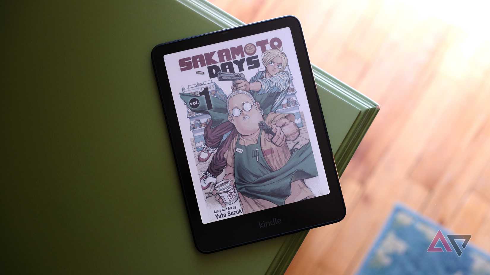 Kindle Colorosoft mostrando o mangá Sakamoto Days na tela enquanto está deitado na beira da mesa