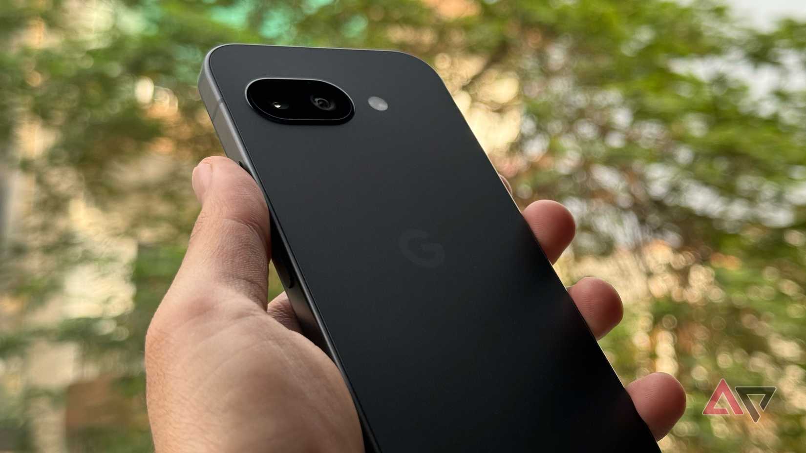 Inquadratura angolata di Pixel 9a nero sollevato all'aperto che mostra il design del retro