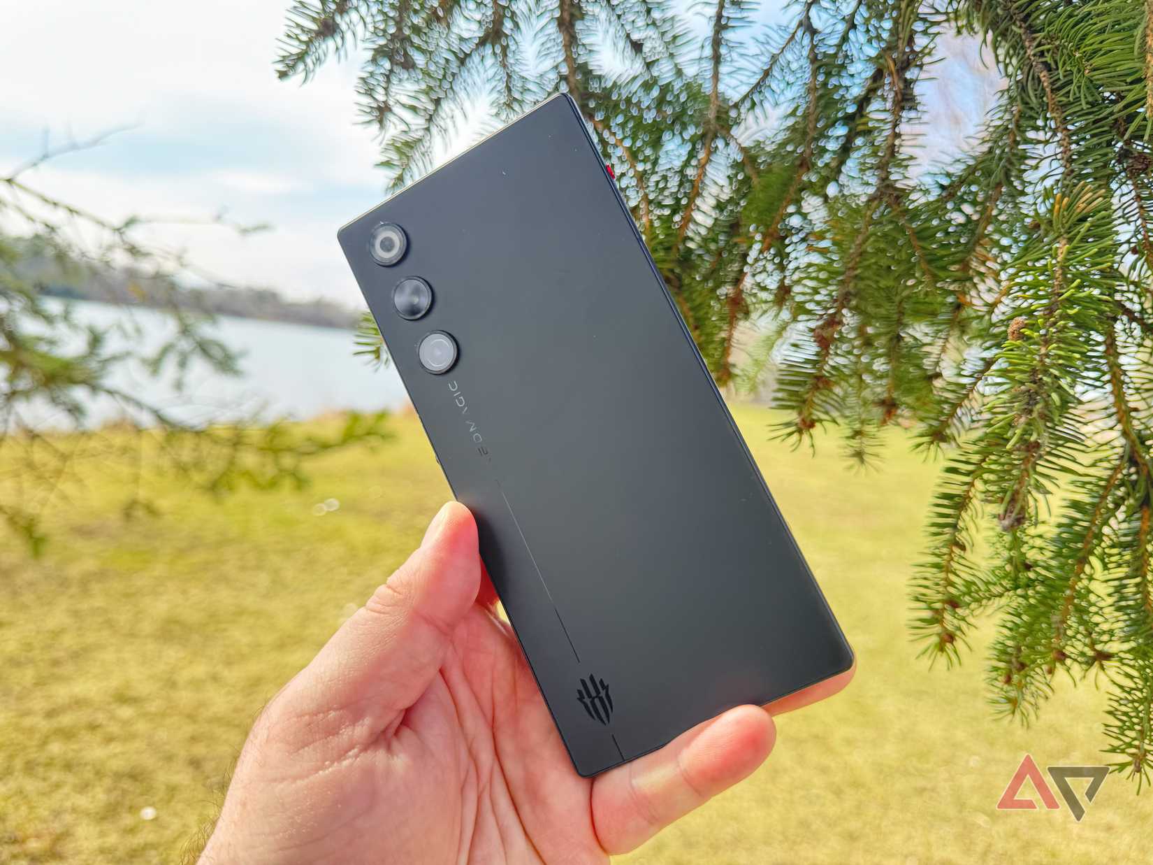 Redmagic 10 black air held in hand with a tree and herbal field in the background. 