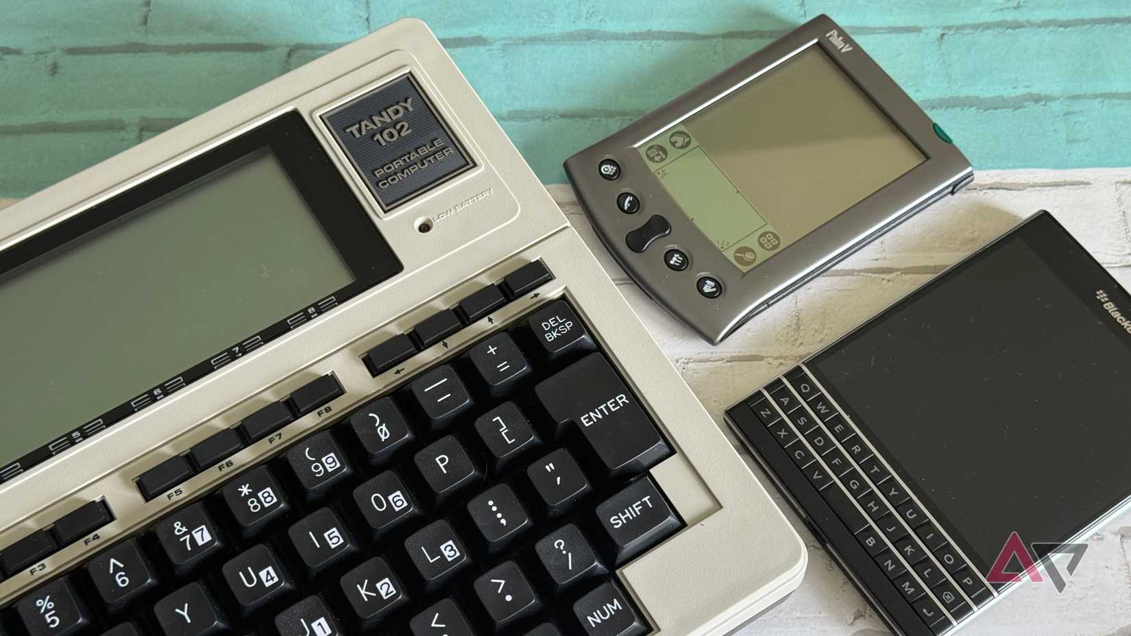 Un Tandy 102, un BlackBerry Passport e un Palm V appoggiati su una scrivania