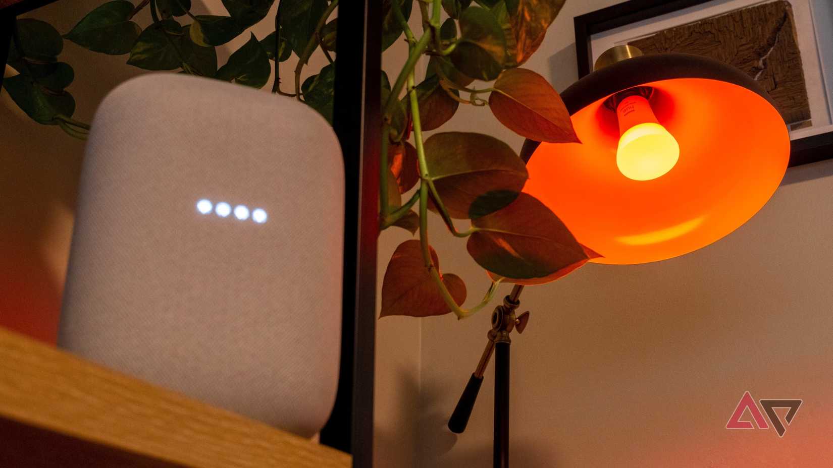 Um alto-falante Nest Audio e uma lâmpada colorida Philips Hue ao lado de uma planta.