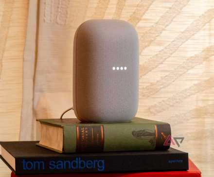 The Nest Audio speaker with its lights active, sitting on a small pile of books