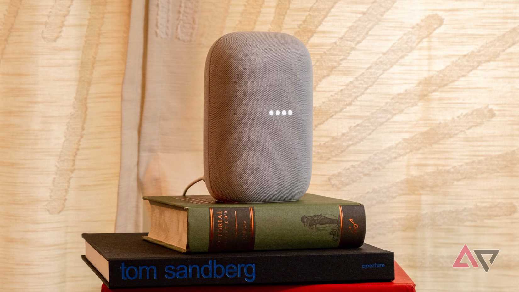 O alto -falante do Nest Audio com suas luzes ativas, sentado em uma pequena pilha de livros