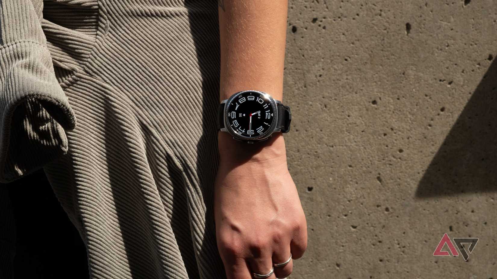 O Samsung Galaxy Watch 8 Classic em um pulso em frente a uma parede de concreto