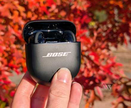 Bose QuietComfort Ultra earbuds in case, held up with fall foliage in background