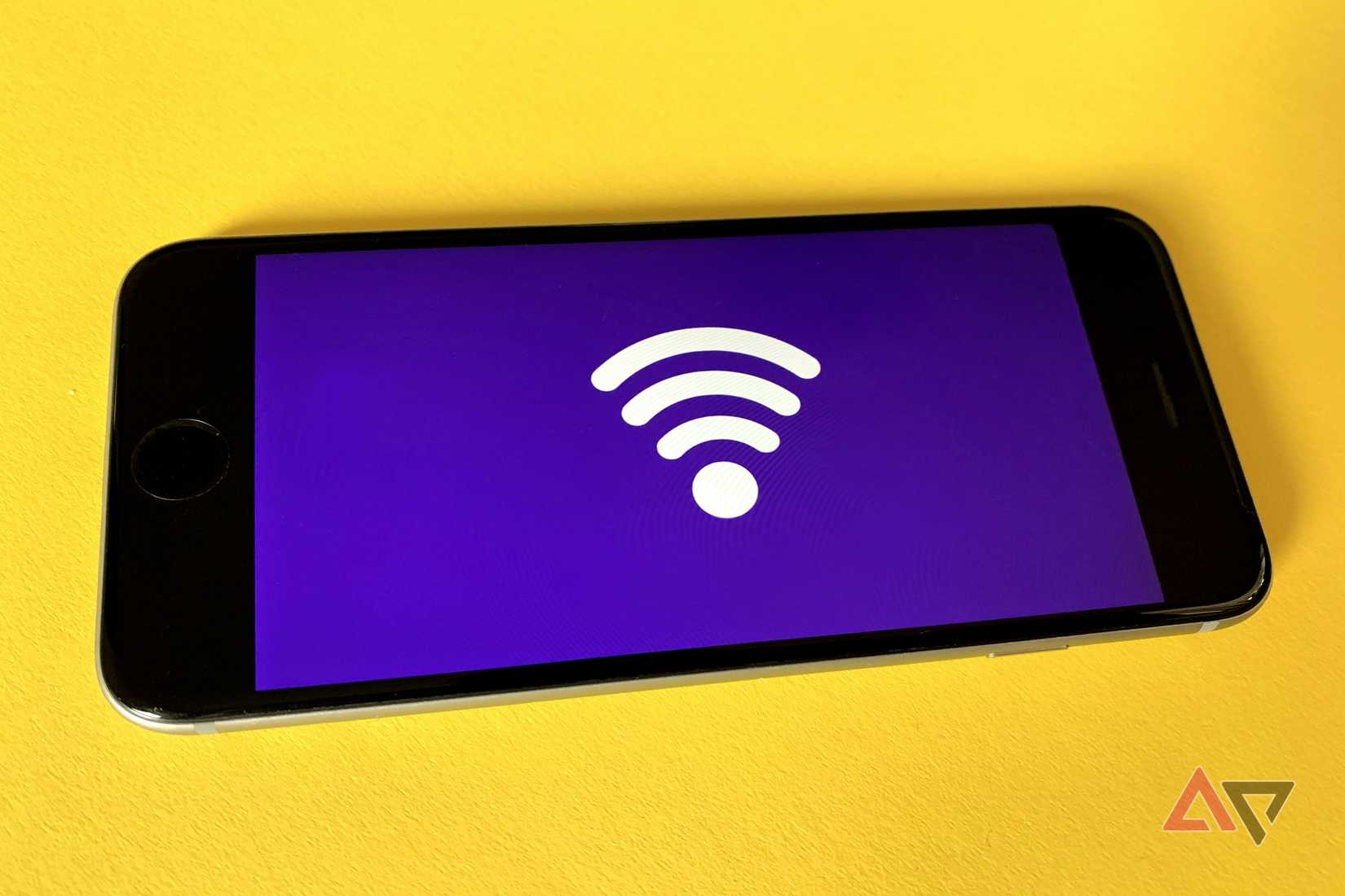 Um smartphone em uma superfície amarela exibindo um grande ícone de Wi-Fi branco sobre um fundo índigo