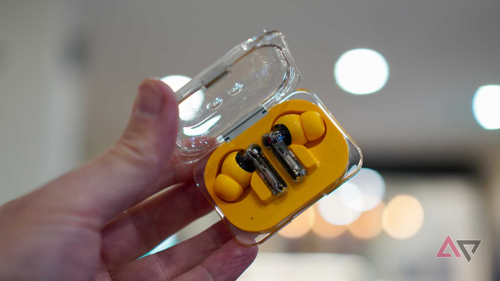 Una persona che tiene in mano gli auricolari e la custodia Nothing Ear (a).