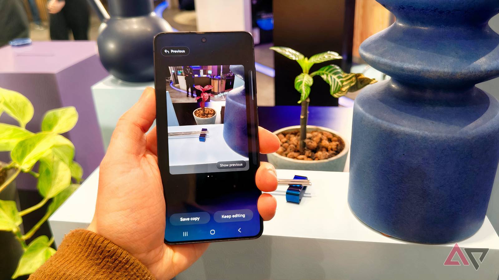 The Samsung Galaxy S26 in a man's hand, showing Generative Edit which has turned a plant's leaves red in a photo.