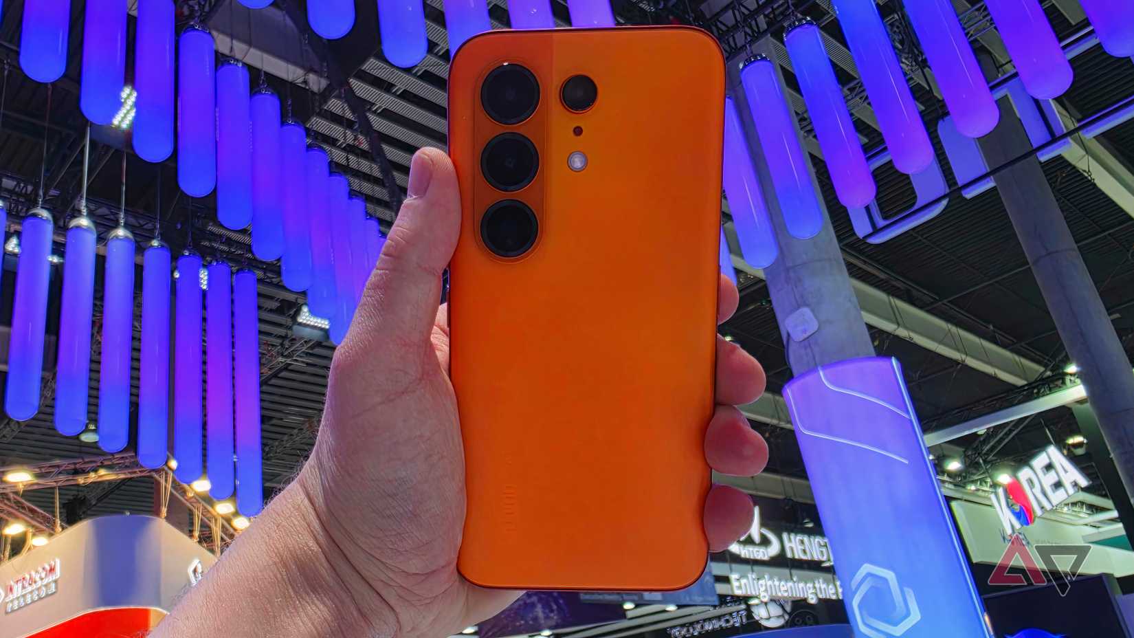 O modelo laranja Tecno Camon 50 Pro na mão de um homem, em frente a algumas luzes azuis.