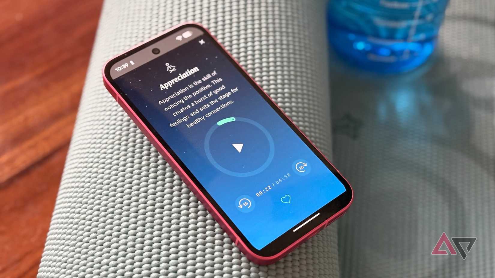 Um telefone rosa exibindo o aplicativo de meditação Healthy Minds em um tapete de ioga azul