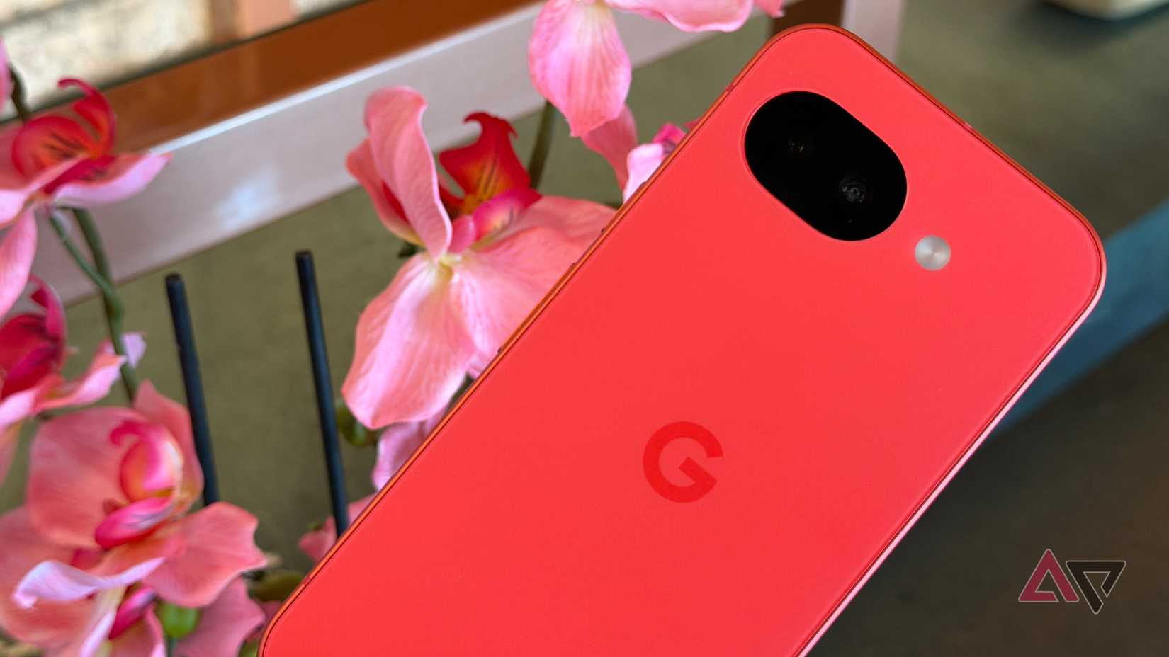 Google Pixel 10a em Berry ao lado de flores rosa