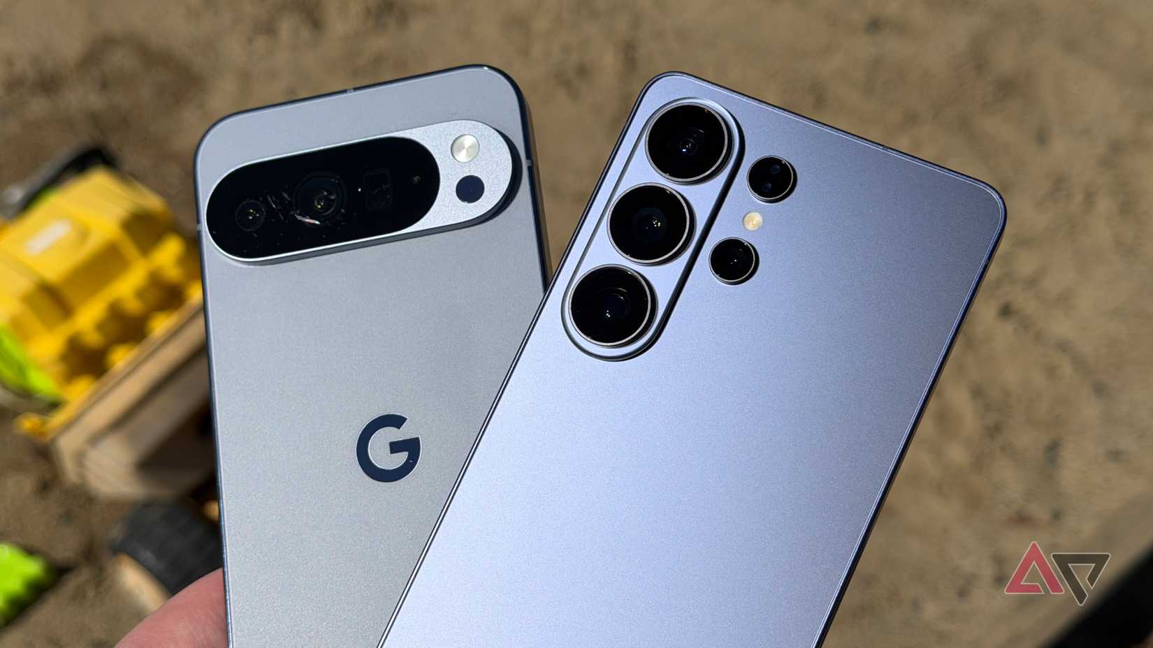 Galaxy S26 Ultra e Pixel 10 Pro XL segurados em um dia ensolarado em uma caixa de areia