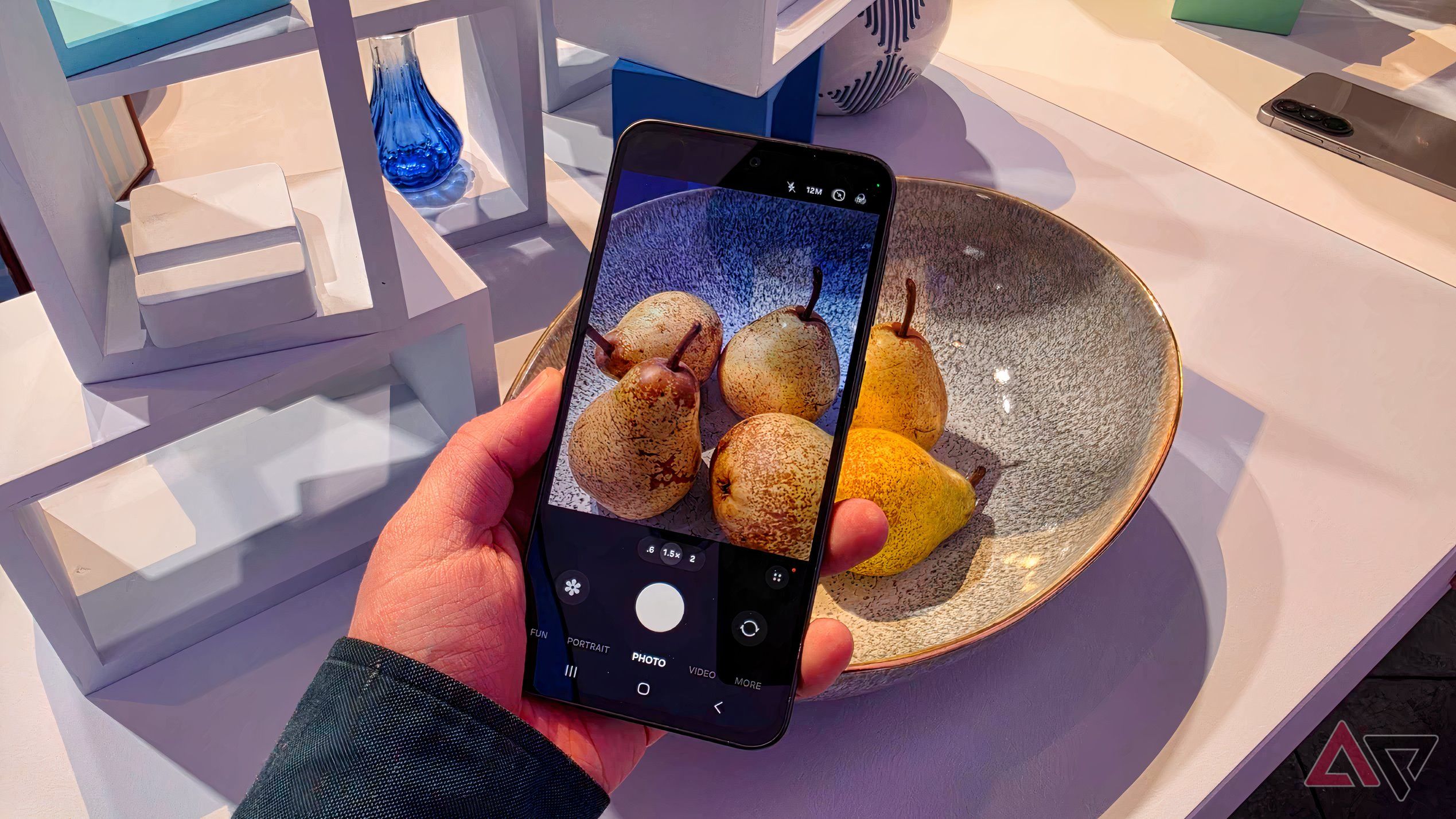 The Samsung Galaxy A37 in a man's hand, showing the camera viewfinder pointed at a bowl of pears.