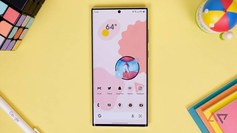 An Android phone against a yellow background with various items around it. 