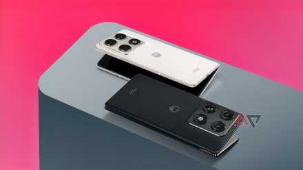 Two Motorola Razr Fold smartphones, one in Lily White and one in Blackened Blue, resting on a grey surface against a pink background.