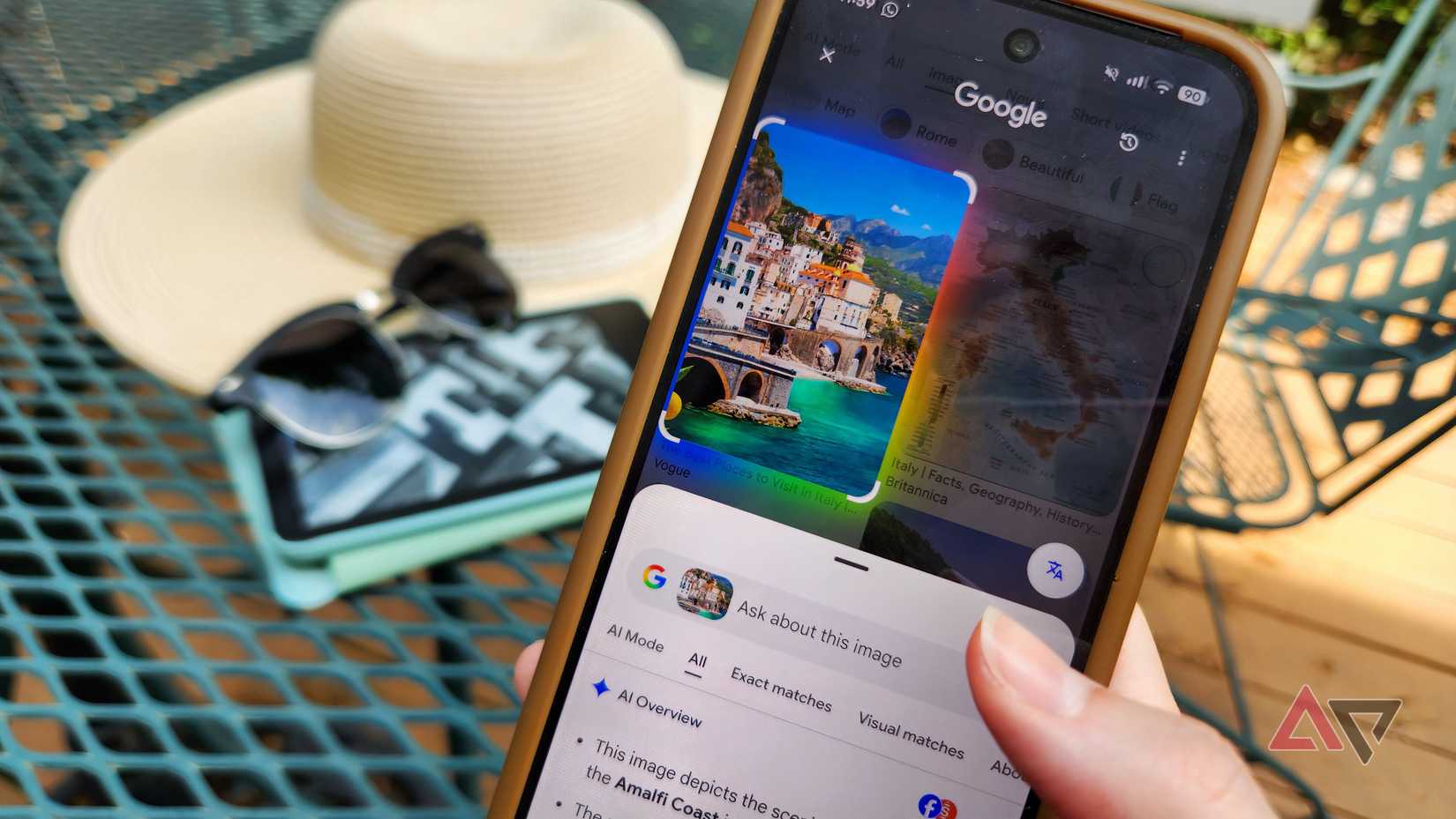 Google Pixel 9 showing a search result for Italy with sunglasses and a hat in the background.