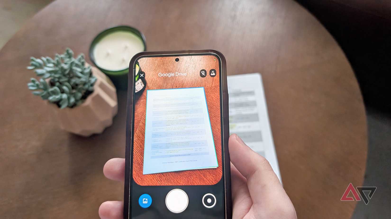 A hand holding a phone that is scanning a document on a brown table