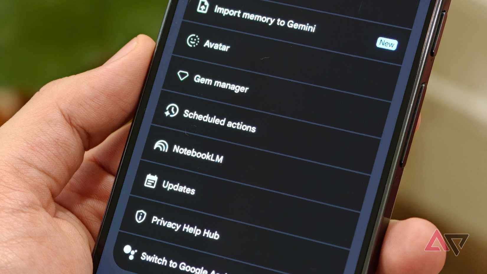 Uma mão segurando um smartphone mostrando a lista de configurações do Google Gemini destacando a opção Ações agendadas abaixo do Gem Manager