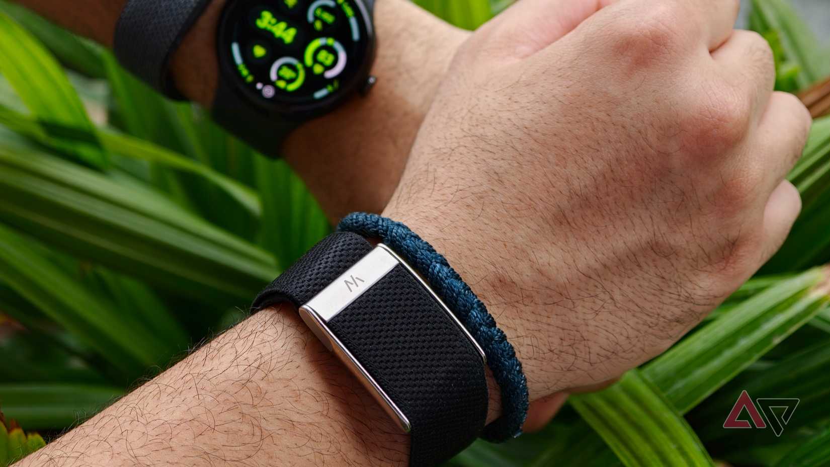 Close-up focus on a Whoop fitness tracker band on a wrist with its metallic clasp visible, while a Google Pixel Watch is blurred in the background