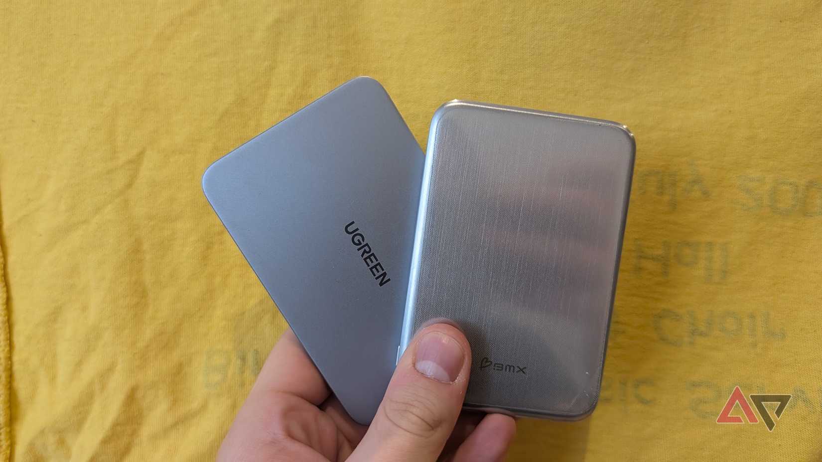 two silver power banks held in hand against a yellow background