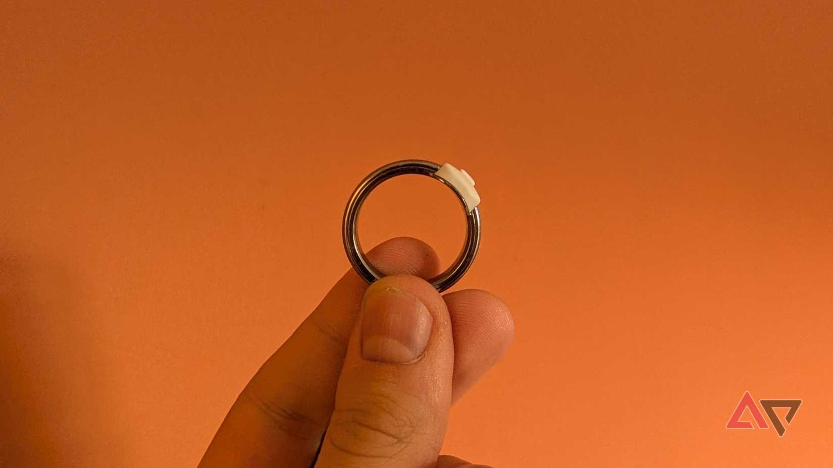hand holding silver ring in front of orange background