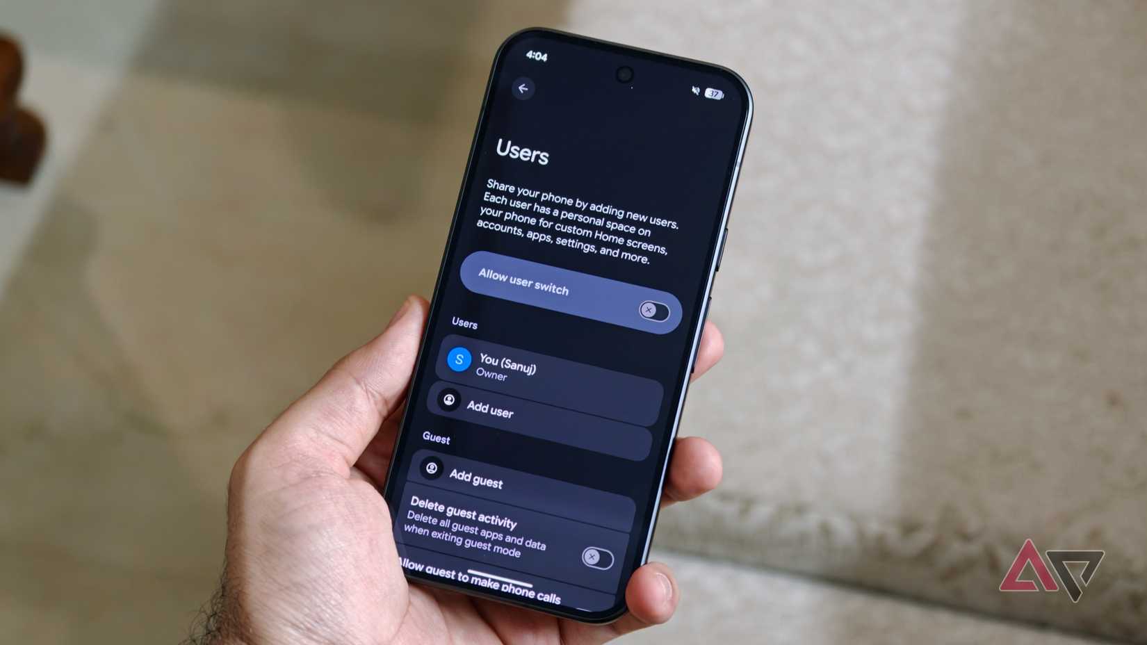A hand holding a Pixel phone showing the Android Users settings page with options to allow user switching