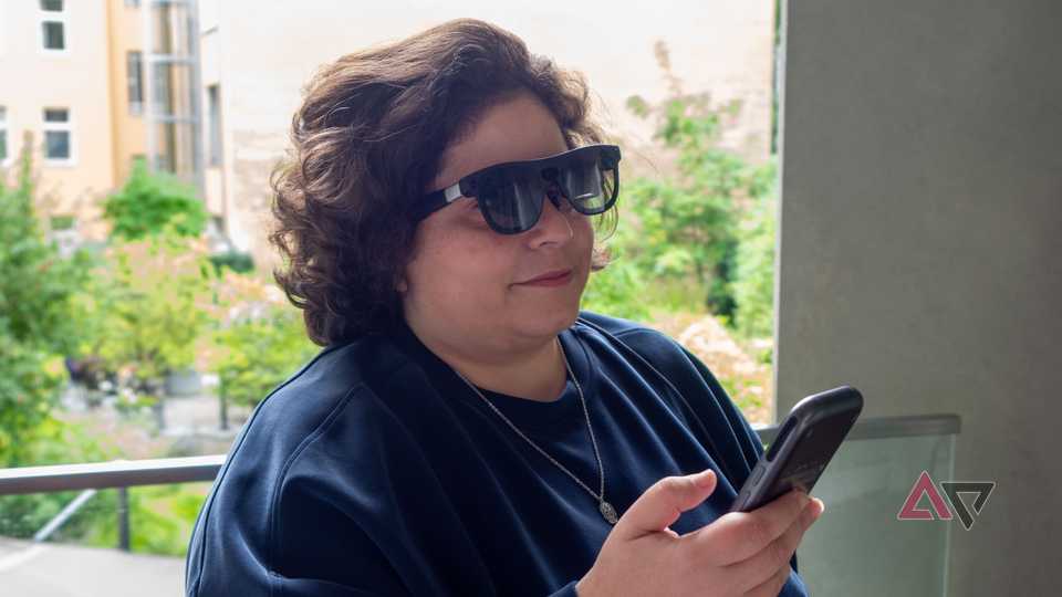 Xreal Aura glasses worn on face, with the main unit in the hand